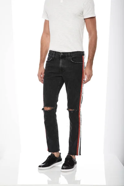 Nenáročné černé tenké fit pánské džínsy s tenisky s bílým pozadím, Classic pánské bílé tričko s pruhovaným kolenem střižené kalhoty spárované s černými tenisky s bílým pozadím — Stock fotografie