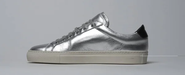 Beyaz zemin ve beyaz arka planı olan parlak gümüş renkli spor ayakkabılar. — Stok fotoğraf