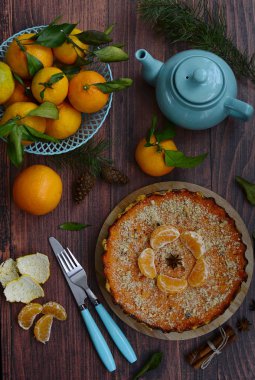 Turtanın üst görüntüsü, mavi sepetlerin içindeki mandalinalar, çaydanlık, kozalak, çatal ve bıçak ahşap bir masada.