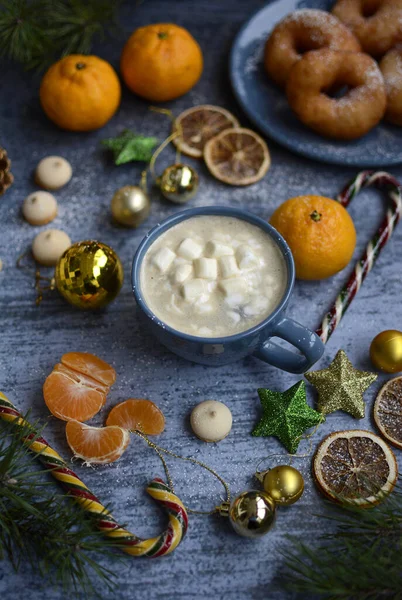 Christmas composition on a blue background from Christmas balls, candies, tangerines, coffee mugs and marshmallows, donuts and fir branches — Stock Photo, Image