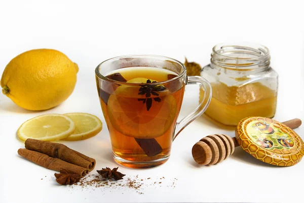 Skleněné hrnky s čajem, skořicí, plátky citronu, sklenice medu, skořicové tyčinky na bílém pozadí — Stock fotografie