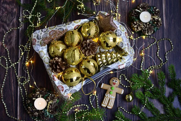 Christmas composition. Golden balls in a box, Christmas beads, garlands, candles in decorative candlesticks on a dark wooden background