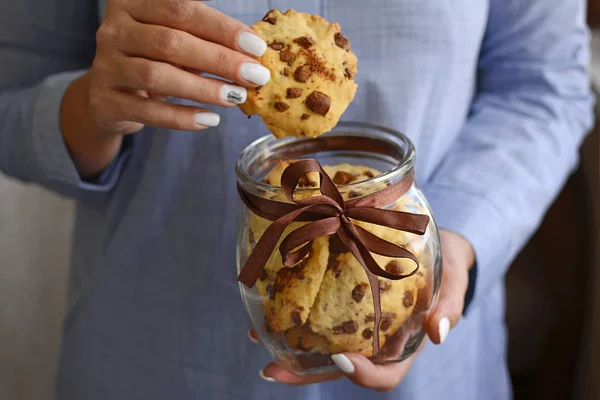 Female hand pulls cookies out of a glass jar with a brown ribbon and delicious homemade cookies.