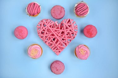 Açık mavi arka planda hasır pembe kalp ve pembe kekler, manzara