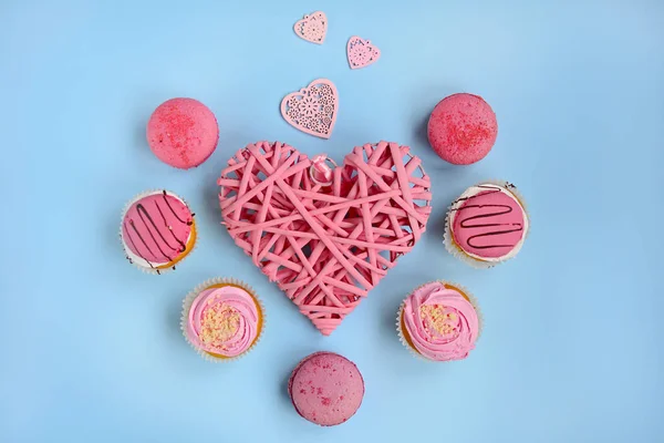 Layout for Valentine\'s Day. Wicker pink heart and pink cakes on a light blue background, view