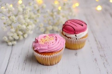 İki pembe lezzetli kek ve beyaz narin çiçekler açık ahşap arka planda.