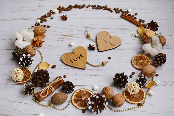 Ghirlanda di coni, fette d'arancia, noci, fiori di cotone, fiori secchi e chicchi di caffè con cuori di legno su uno sfondo leggero. Concetto di San Valentino — Foto Stock