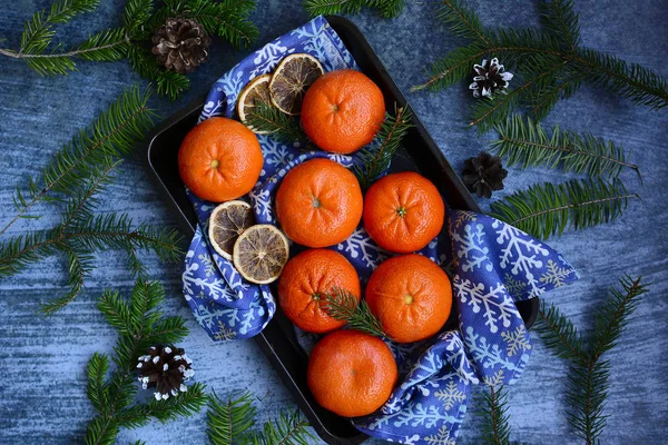 Orange juicy ripe tangerines and spruce branches on a blue background. — Stock Photo, Image