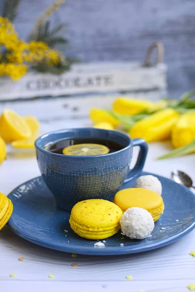 Tazza di tè blu con limone, amaretti gialli, tulipani e rami di mimosa su fondo chiaro. Riposo domestico . — Foto Stock