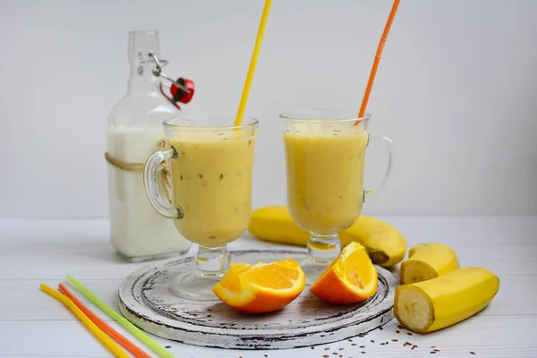Orange-banana smoothie, a bottle of milk, slices of orange and banana and multi-colored tubules on a white background. Close-up