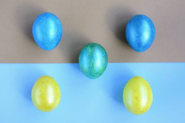 Sarı, mavi ve turkuaz yumurtalar açık mavi ve altın sarısı kağıdın üzerinde bulunur. Yukarıdan bak. Paskalya.