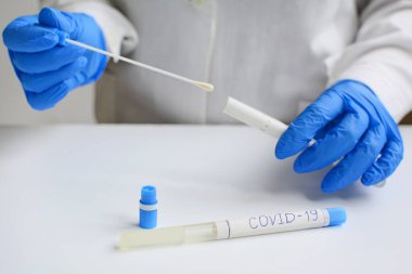 Kovid-19. Mavi eldivendeki ellerde, koronavirüsün yeni viral enfeksiyonunu teşhis etmek için bir mukus örneği var. Kapat.