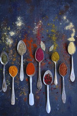 Zerdeçal, zencefil, zira, paprika, sumac ve koyu mavi arka planda metal kaşıklar üzerinde otlar. Dünyanın baharatları işte. Dikey