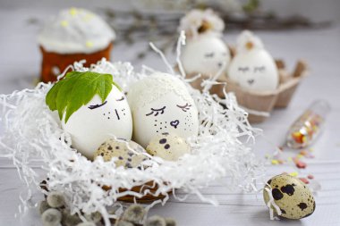 Paskalya konsepti. Süslü kağıt yuvalarda boyanmış gözleri olan beyaz yumurtalar ve hafif ahşap arka planda Paskalya pastası..