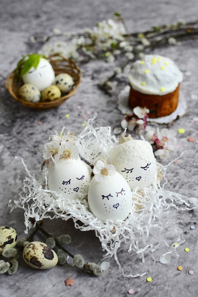 Composizione pasquale di uova bianche con facce dipinte, torta pasquale e ramoscelli di salice su sfondo grigio macchiato. Verticale — Foto Stock