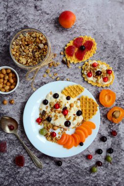 Granola, yoğurt, böğürtlen ve waffle ile kahvaltı gri mermer arka planda beyaz bir tabakta. Yukarıdan görüntüle.