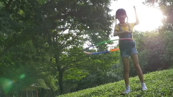 Slow motion shot: Menina asiática feliz jogando holahoop colorido no parque com luz do sol — Vídeo de Stock
