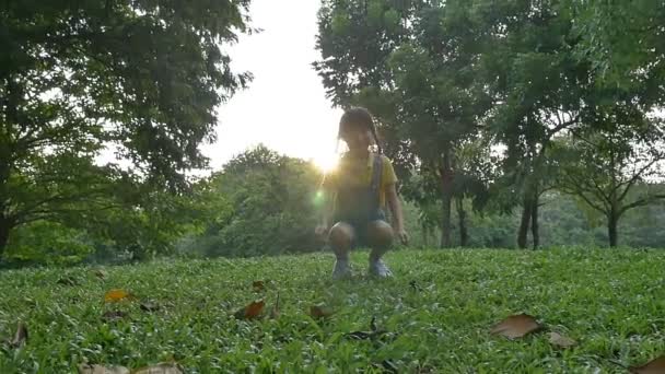 Disparo en cámara lenta: Feliz niña asiática saltando en el parque con la luz del sol — Vídeo de stock