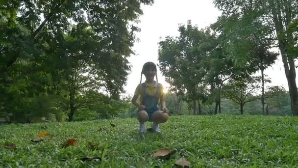 Повільний рух постріл: щасливі азіатські маленька дівчинка, стрибки в парку з сонячного світла — стокове відео