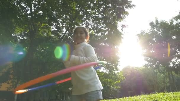 Slow motion shot: Menina asiática feliz jogando holahoop colorido no parque com luz solar — Vídeo de Stock