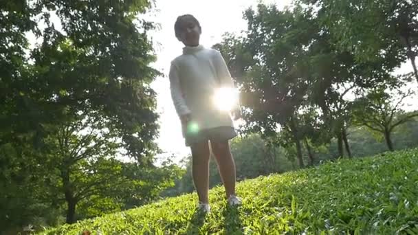 Slow motion shot: Menina asiática feliz pulando no parque com luz solar — Vídeo de Stock