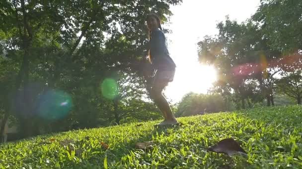 Disparo en cámara lenta: Feliz niña asiática saltando en el parque con la luz del sol — Vídeo de stock