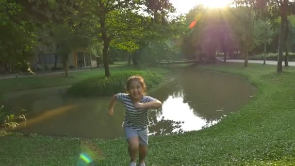 Yavaş çekim: mutlu Asyalı küçük kız parkta güneş ışığı ile çalışan — Stok video