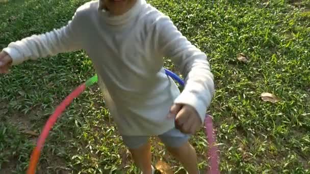 Slow motion shot : Bonne petite fille asiatique jouant holahoop coloré dans le parc avec la lumière du soleil — Video