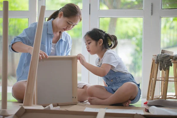 Asiático linda menina ajudando sua mãe montando novo mobiliário DIY em casa juntos — Fotografia de Stock