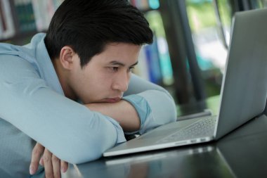 Dizüstü bilgisayar ile uykulu genç bir Asyalı işçi