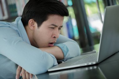 Dizüstü bilgisayar ile uykulu genç bir Asyalı işçi