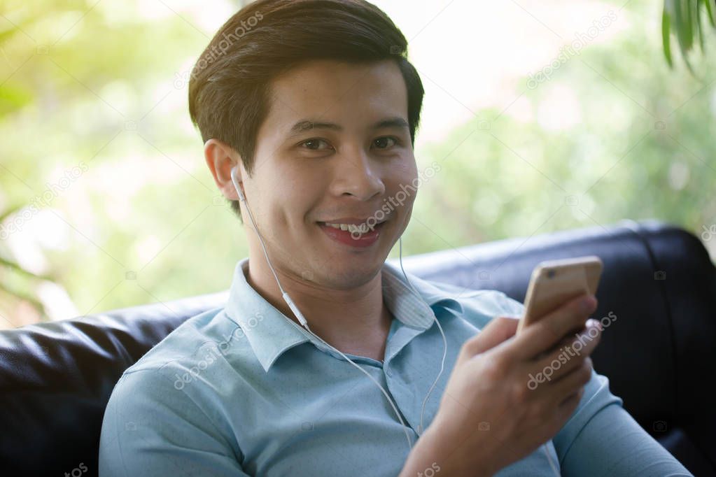 Young Asian man listening music smart phone in cafe