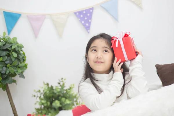 Happy Asian girl shaking a present to guess whats inside — Stock Photo, Image