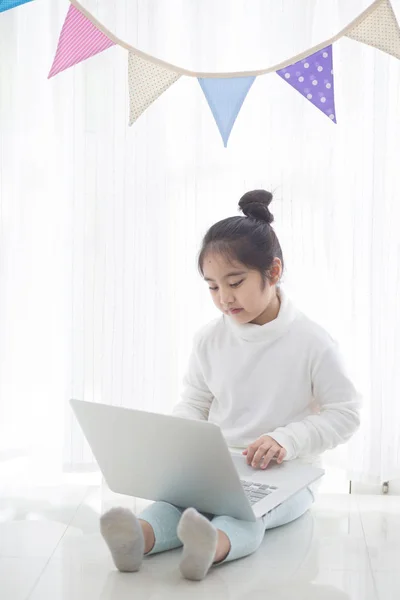 パステル カラーの三角形の党旗の高い重要なプロセスで飾られた部屋でノート パソコンを使用して幸せなアジアの女の子 — ストック写真
