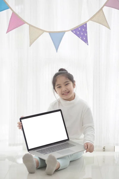 Happy Asian girl showing laptop screen in decorated room with pastel triangle party flag, High key process — Stock Photo, Image