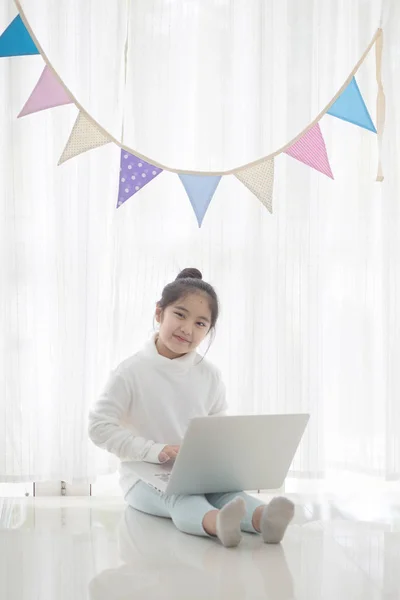 パステル カラーの三角形の党旗の高い重要なプロセスで飾られた部屋でノート パソコンを使用して幸せなアジアの女の子 — ストック写真