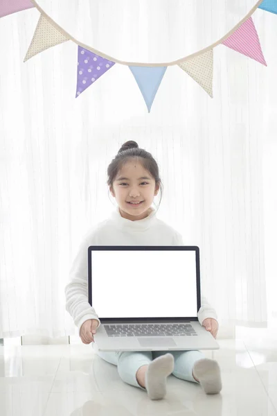 Glad flicka visar laptop skärm i rum inredda med pastellfärgade triangel partifana, hög nyckelprocess — Stockfoto