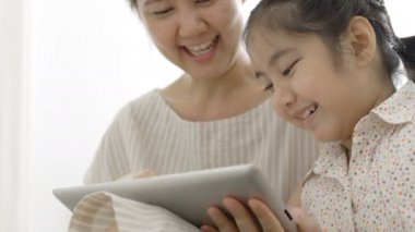 4k: ağır çekim mutlu Asya anne ve kızı dijital tablet ile birlikte evde oynamak