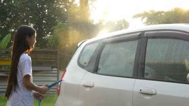 4k: szczęśliwy dziewczyna azjatyckich mycie samochodu na rozbryzgi wody i światła słonecznego w domu — Wideo stockowe