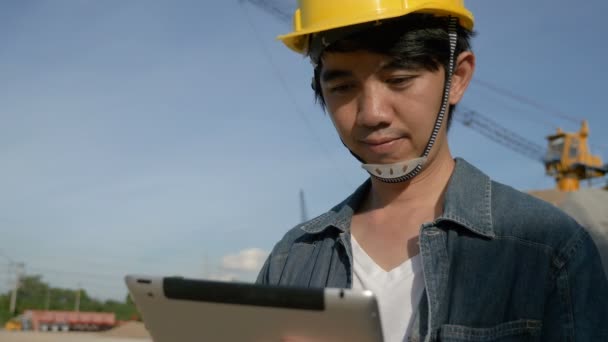 4k: Aziatische ingenieur met behulp van digitale tablet op de bouwplaats met blauwe lucht — Stockvideo