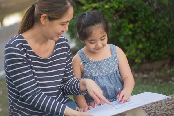 Happy Asian Daughter drawing picture with mother together in the park