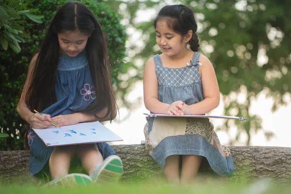 Happy Asian girls enjoying to draw pictures together in park — Stock Photo, Image