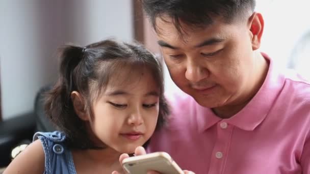 Μικρό ασιατικό κορίτσι που παίζει το παιχνίδι στο κινητό τηλέφωνο με τον πατέρα της — Αρχείο Βίντεο