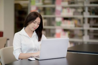 Portrait of a happy beautiful Asian student girl using laptop in a library clipart