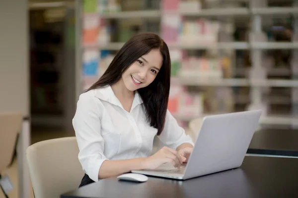 Portrait of a happy beautiful Asian student girl using laptop in a library — Stock Photo, Image