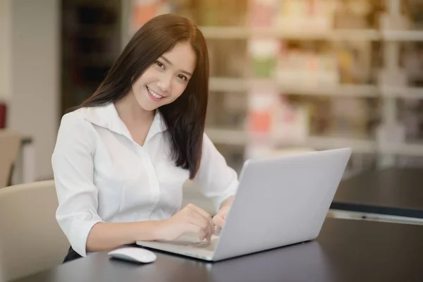 Ritratto di una bella studentessa asiatica felice che usa il computer portatile in una biblioteca — Foto Stock