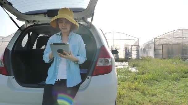 パンショットスマートアジアの女性農家は車の上に座って 緑の家のインターネットアクセスフロントのためのデジタルタブレットを使用して スマート農業の概念 — ストック動画