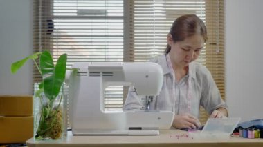 Dolly giyim mağazasında çalışan Asyalı kadını vurdu. Atölyede dikiş makineli Asyalı moda tasarımcısı elbisesi