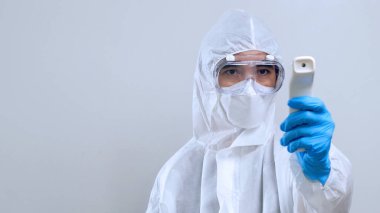 Kızılötesi termometreyle tarama yapan sağlık çalışanı, kızılötesi termometreyle, koruyucu PPE kostümlü ve gözlüklü kendine güvenen Asyalı doktor.