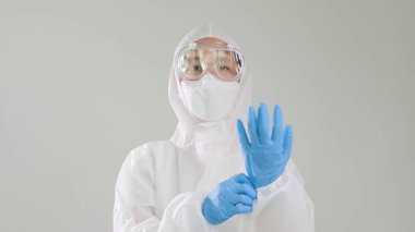 Koruyucu koruyucu koruyucu koruyucu PPE giysili Asyalı doktor tıbbi lateks eldiven giyiyor